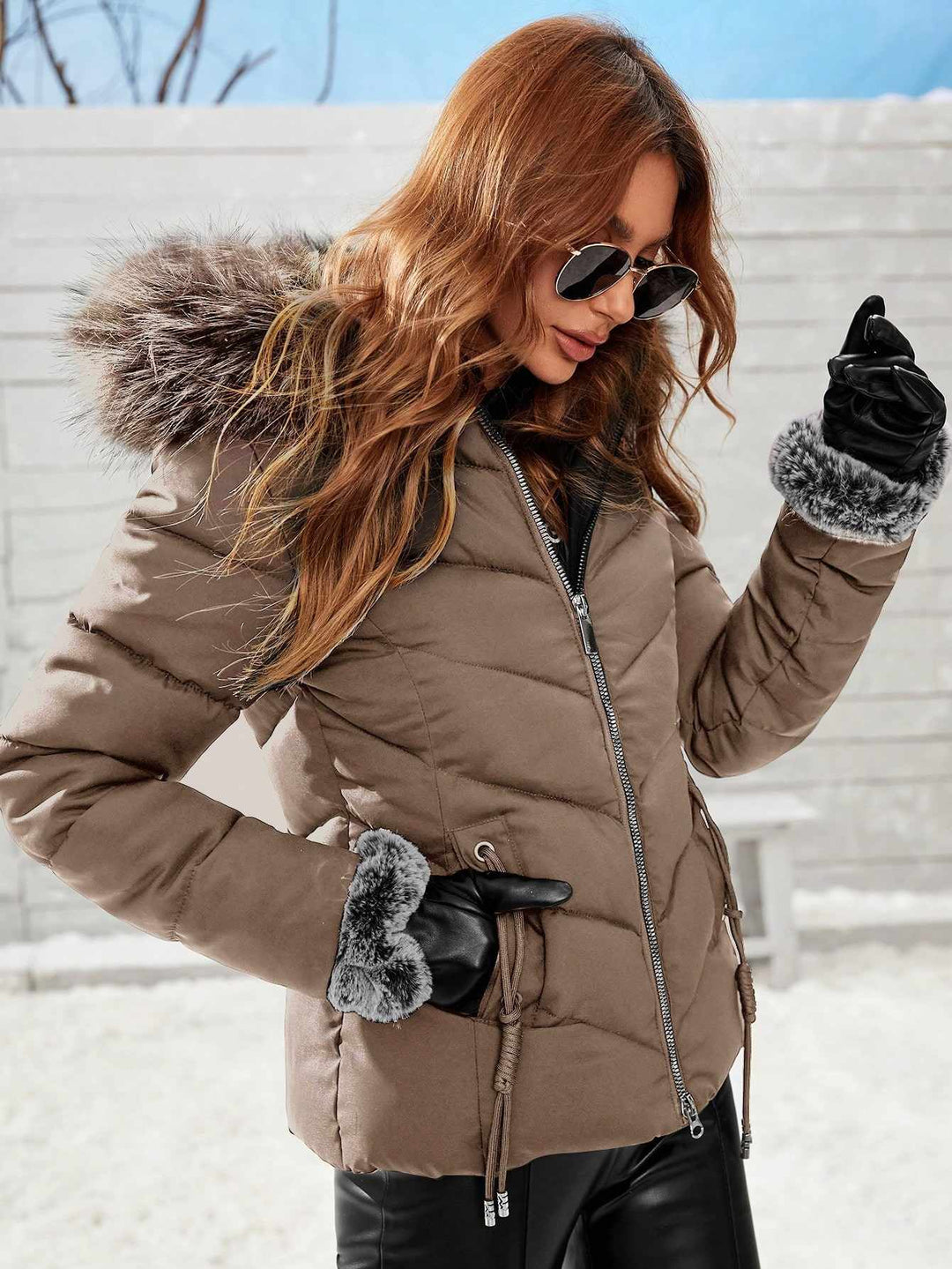 Woman wearing a brown puffer jacket with fur-lined hood and gloves in a snowy setting.