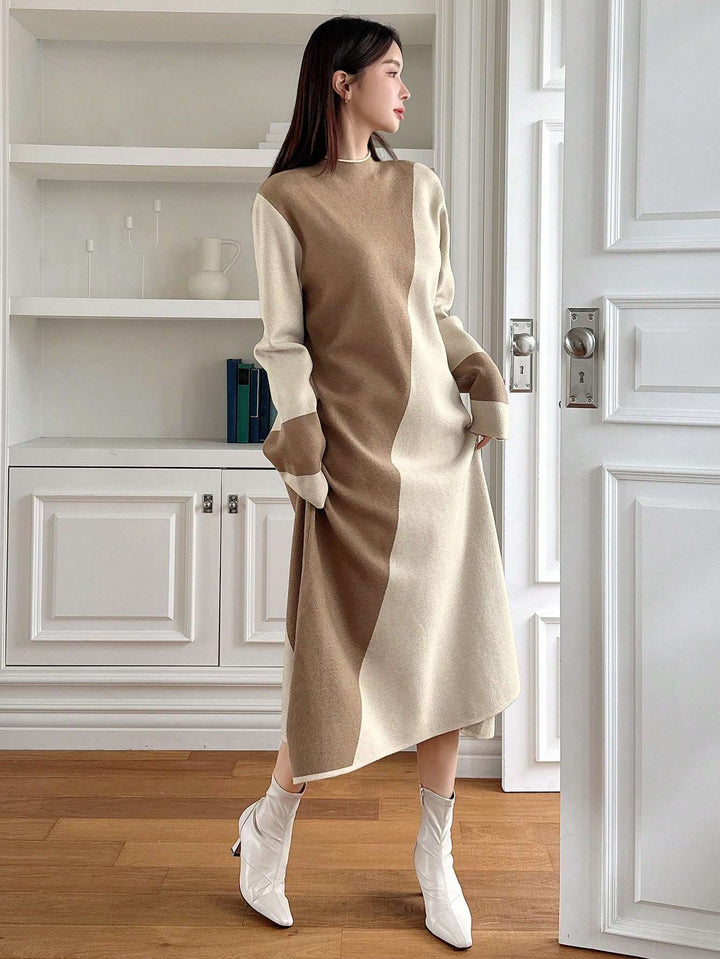 A woman models a long-sleeve color-block knit dress in beige and cream, styled with white ankle boots in a bright, modern room with white cabinetry and wood floors.