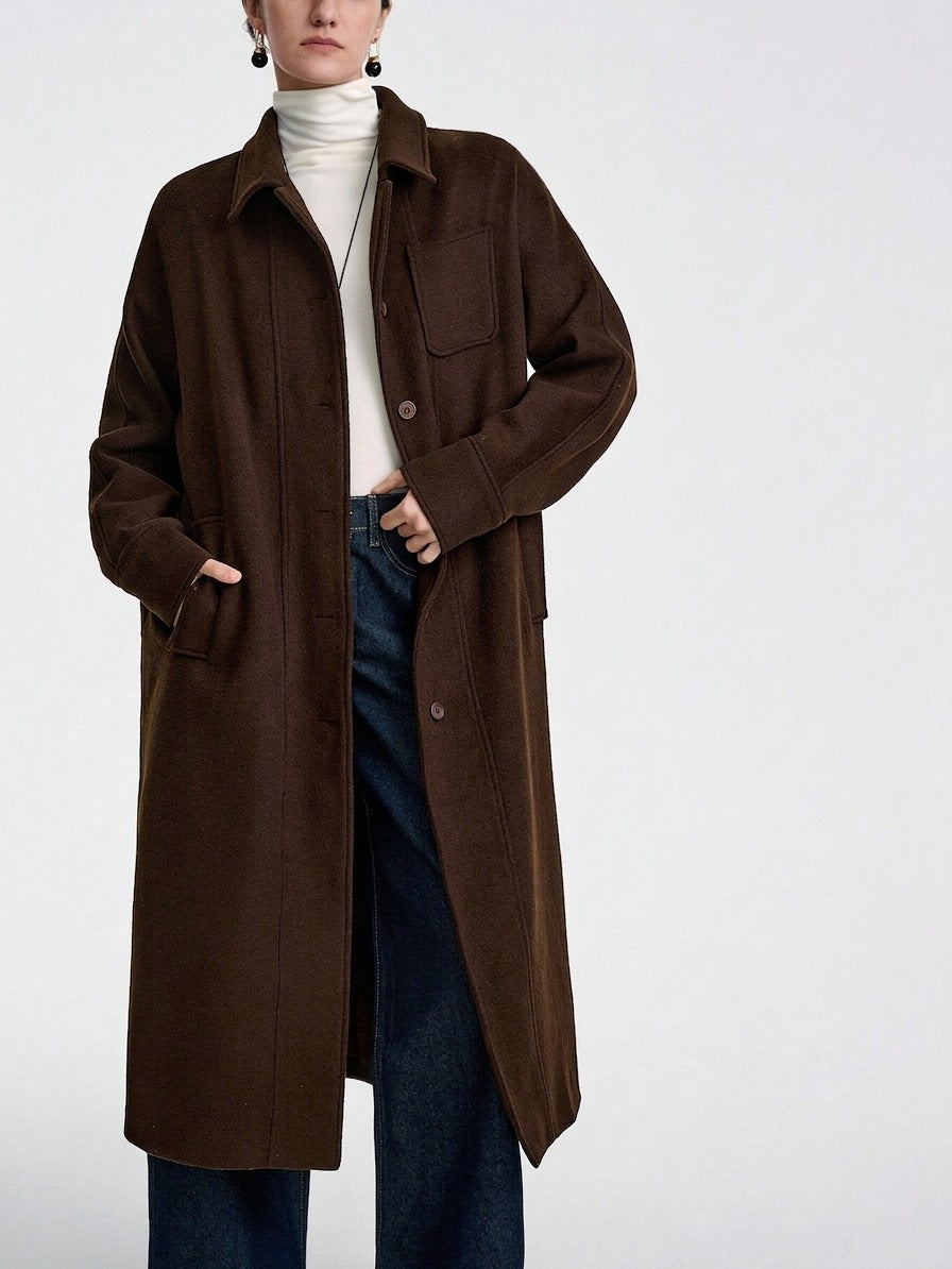 A model wearing a long, dark brown button-up coat over a white turtleneck sweater and blue jeans, photographed against a clean white studio background.