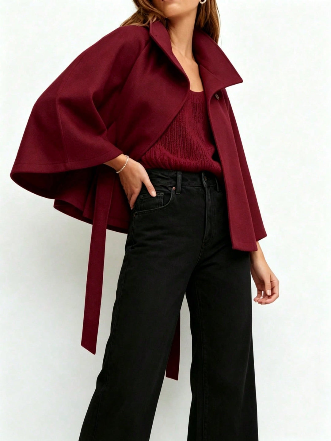 A woman wearing a deep burgundy cape-style wrap coat over a matching ribbed knit top and black wide-leg jeans, photographed against a plain light background.