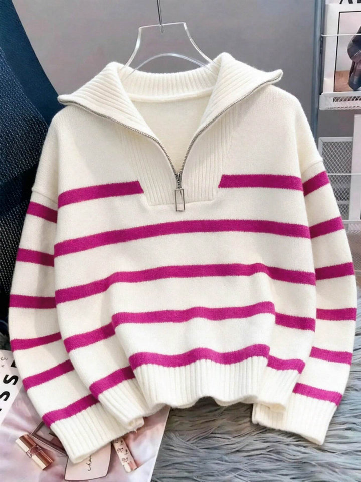 A cream-colored knit half-zip sweater with horizontal magenta pink stripes, hanging on a clear plastic hanger against a gray background.