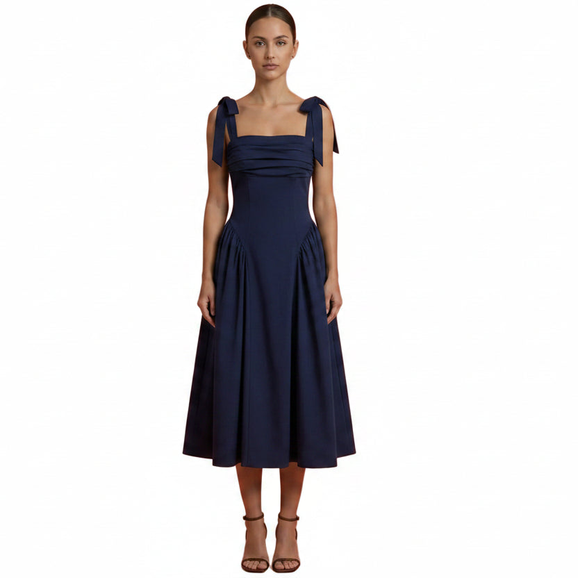 Woman wearing a navy blue dress with bow straps on an orange background