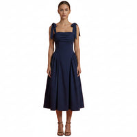 Woman wearing a navy blue dress with bow straps on an orange background